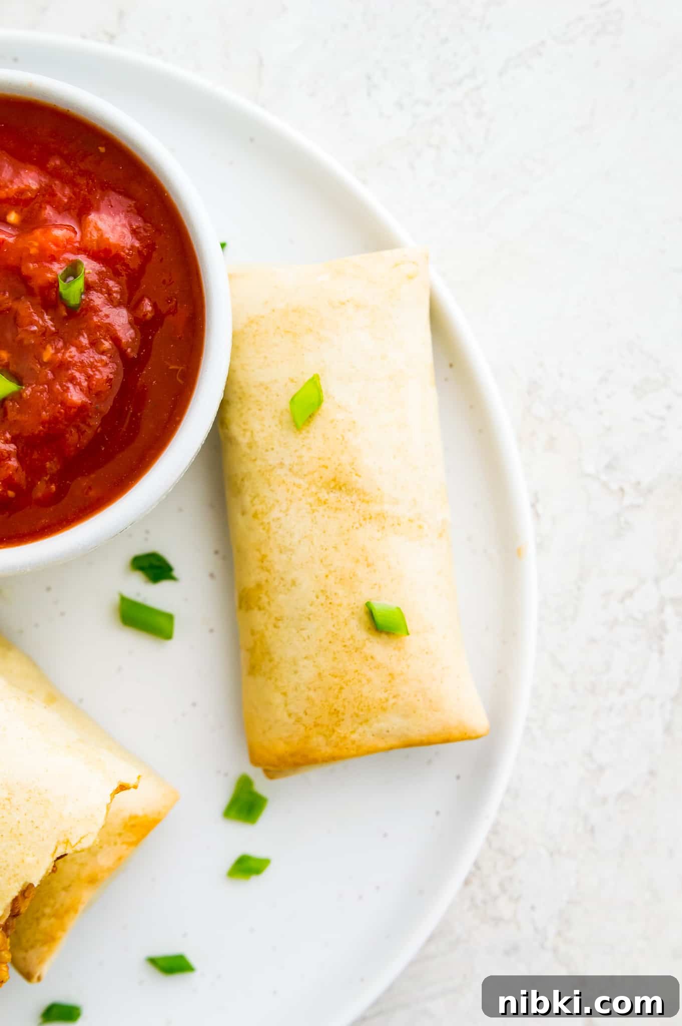 How to Air Fry a Frozen Burrito for Crispy Results 4 A cooked burrito on a plate with a bowl of salsa beside it.