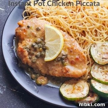 chicken piccata on a black plate with piccata sauce, lemon, noodles & zucchini