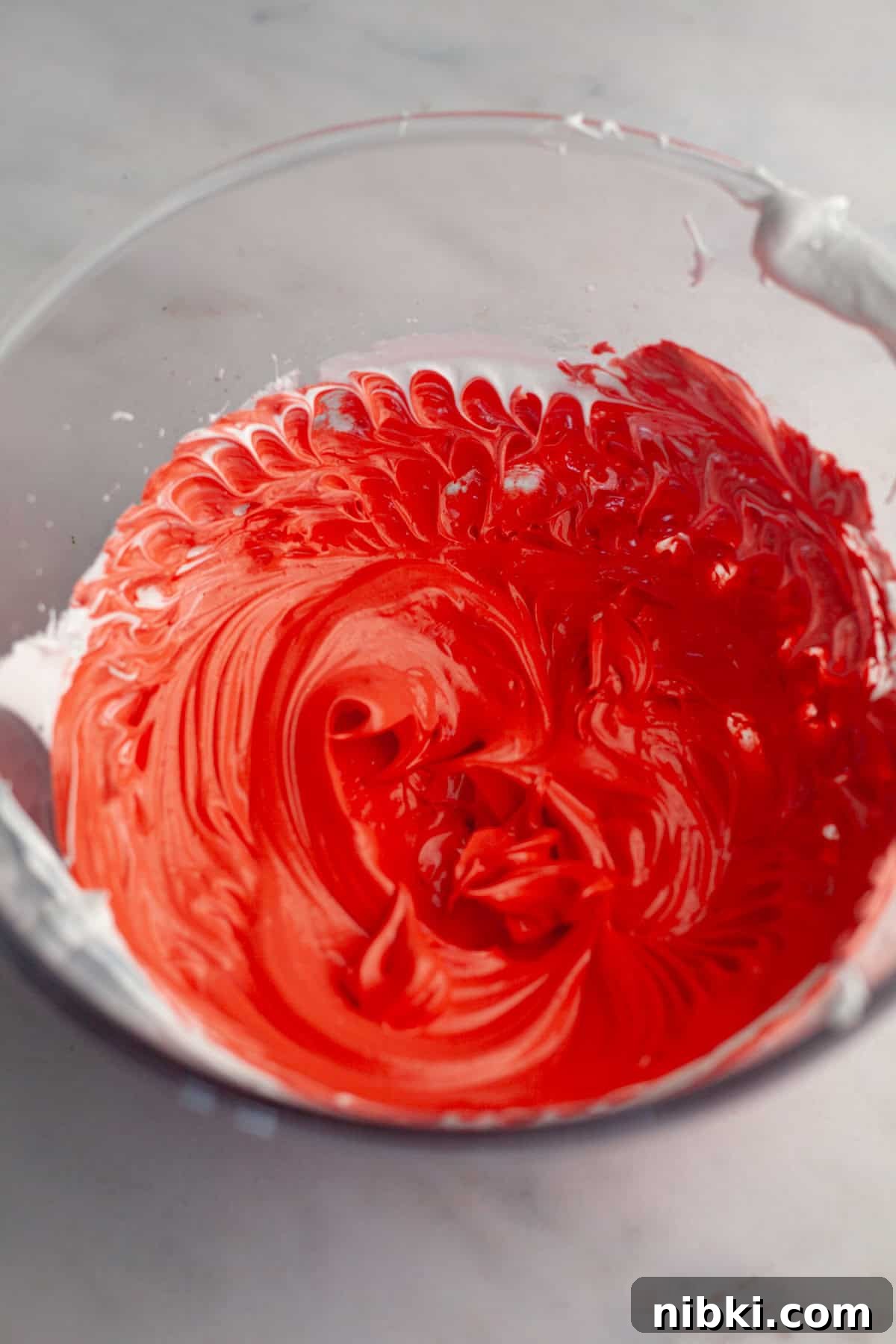 Red glossy meringue batter in a glass bowl.