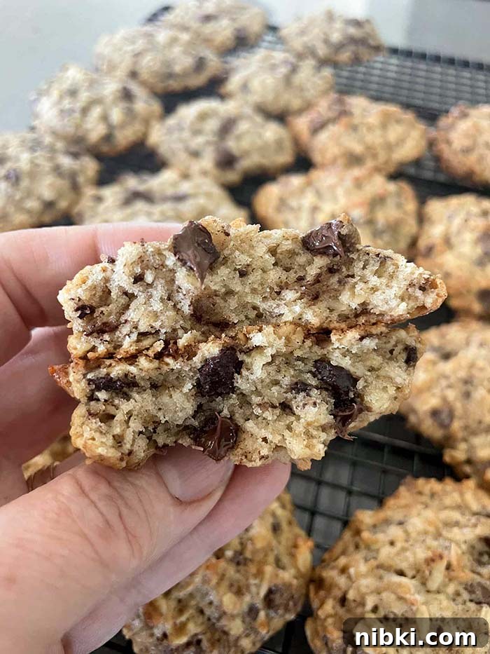 A banana oatmeal cookie broken in half held above a cooling rack of banana oatmeal cookies.