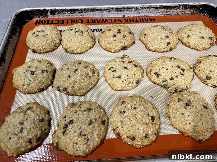 A cookie sheet lined with a silicone baking mat filled with baked banana oatmeal cookies with chocolate chips.