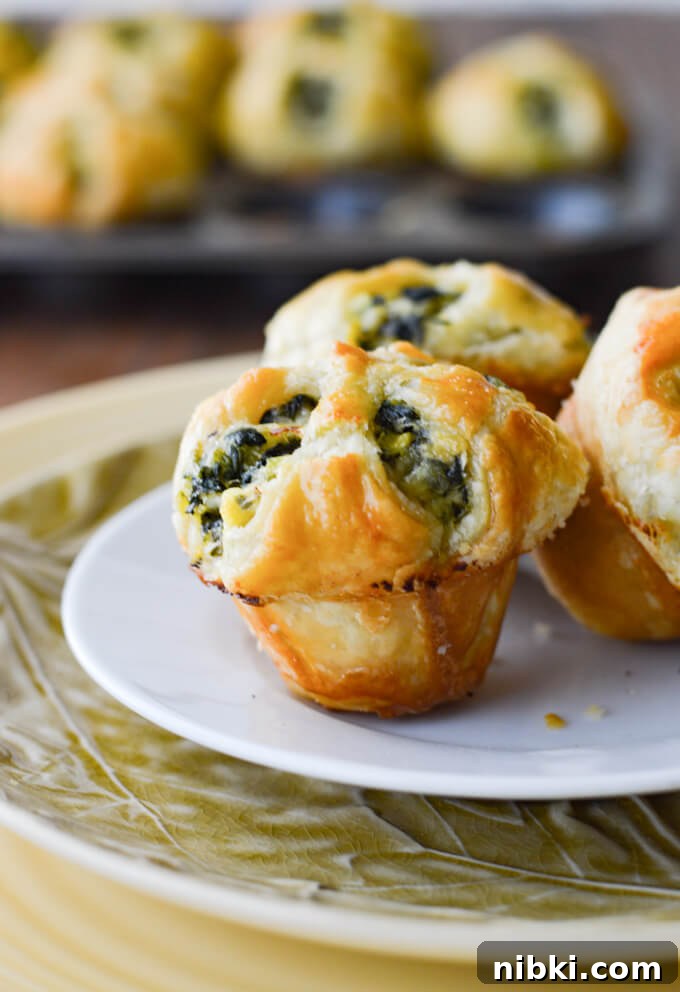 Spinach Puffs Recipe: Flaky Puff Pastry Bites 2 Three spinach stuffed puff pastry appetizers with more appetizers in a muffin tin in the background.
