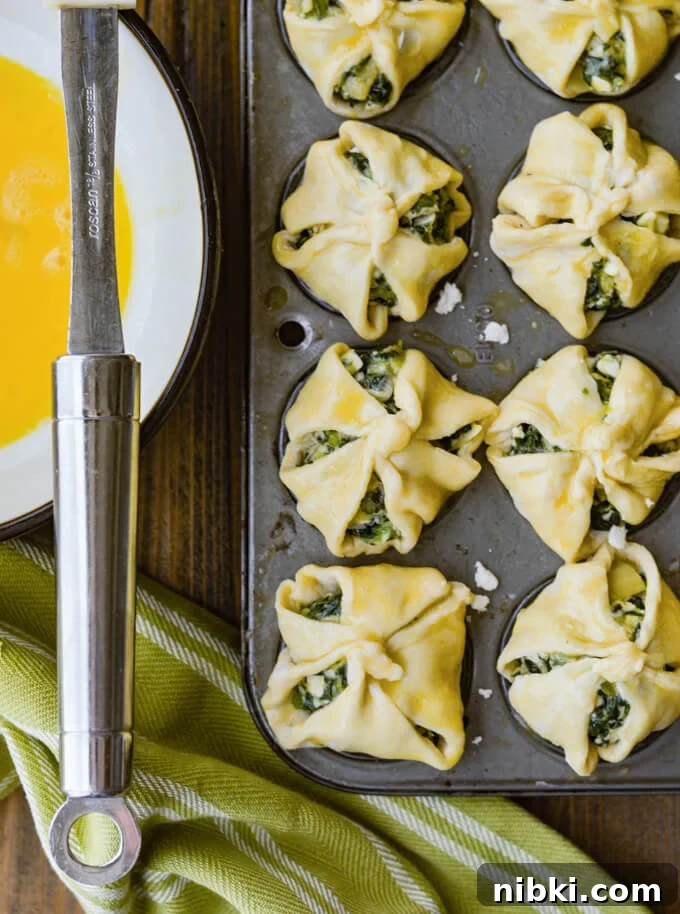 Spinach Puffs Recipe: Flaky Puff Pastry Bites 5 Unbaked puff pastry with spinach filling in mini muffin tins with egg wash on them a green and white napkin beside it and a bowl of egg wash