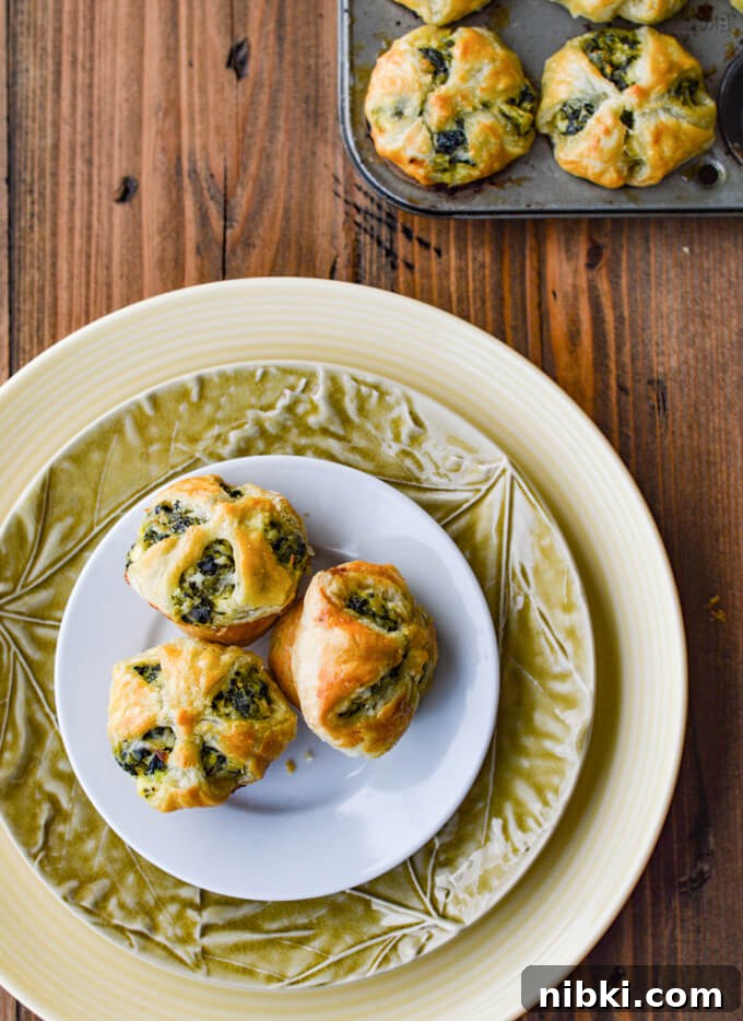 Spinach Puffs Recipe: Flaky Puff Pastry Bites 7 Three Spinach and Feta Puff Pastry Appetizers sitting on several stacked plates. A mini muffin tin is in the corner with spinach puffs in them.