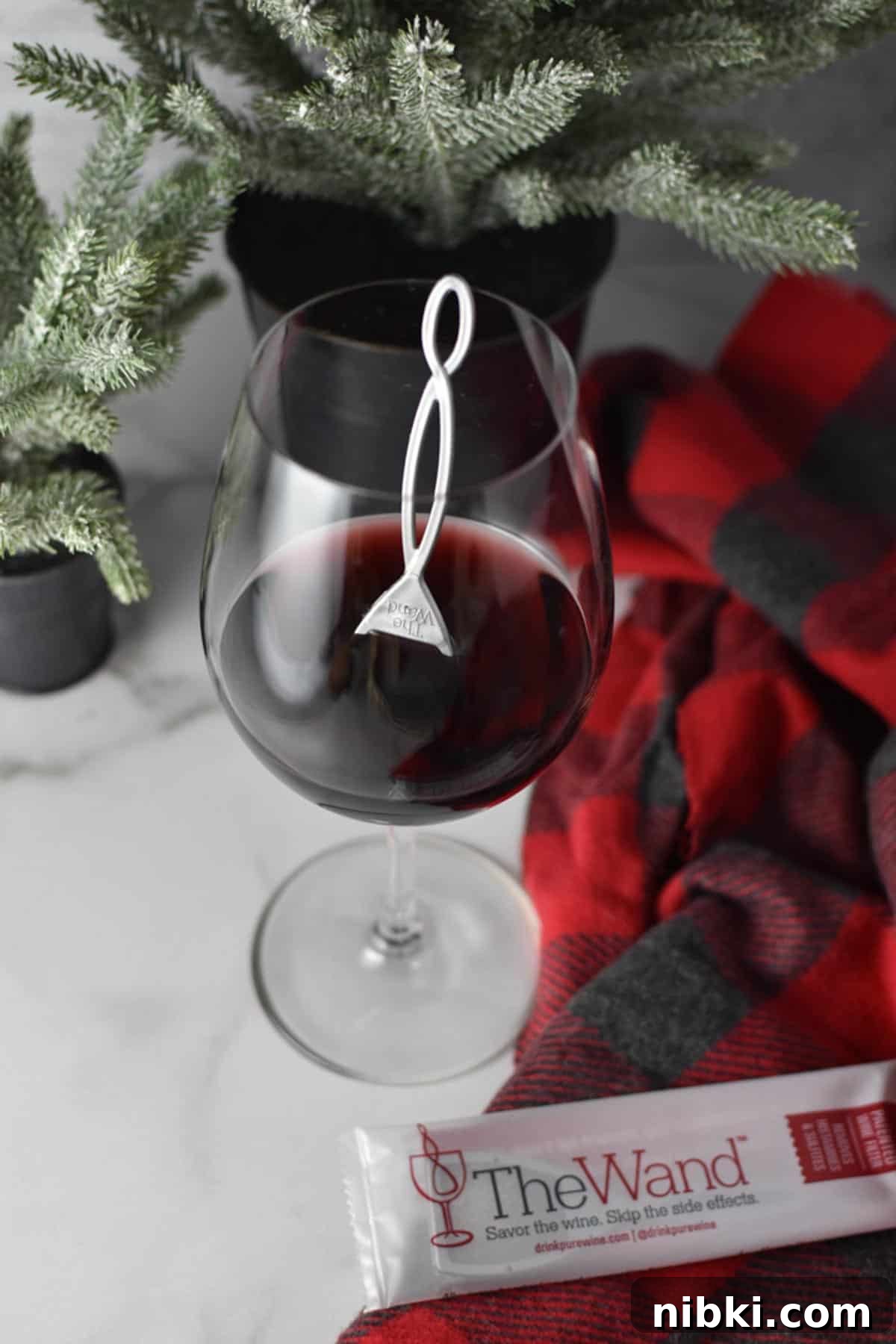A glass with red wine and a wine wand inside of it next to a small tree.