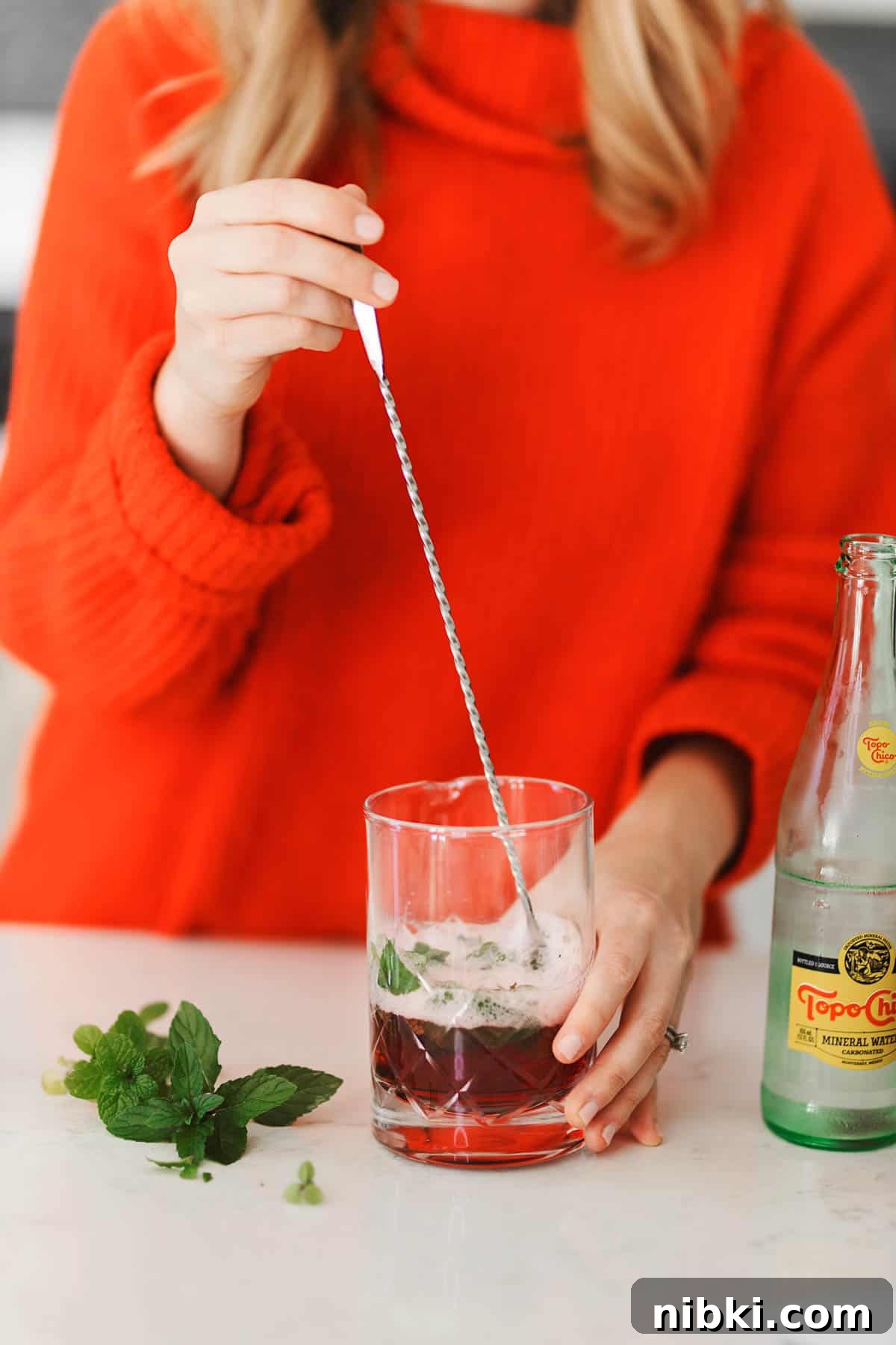 A woman in a red sweater using a mixer to stir juice and sparkling water.