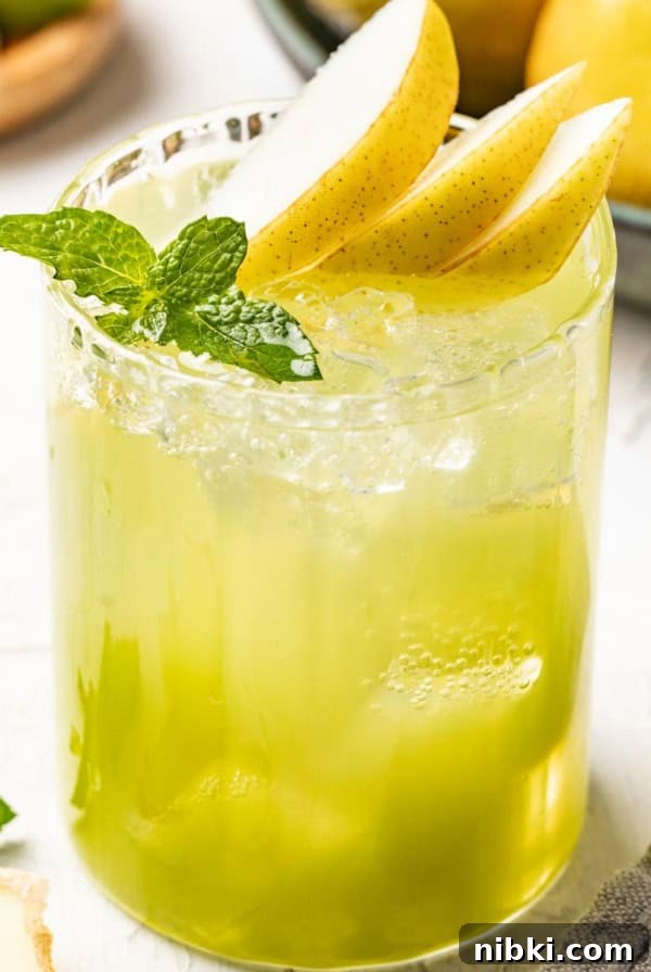 A pear mocktail topped with slice pears and fresh mint in a tall, clear glass with ice.