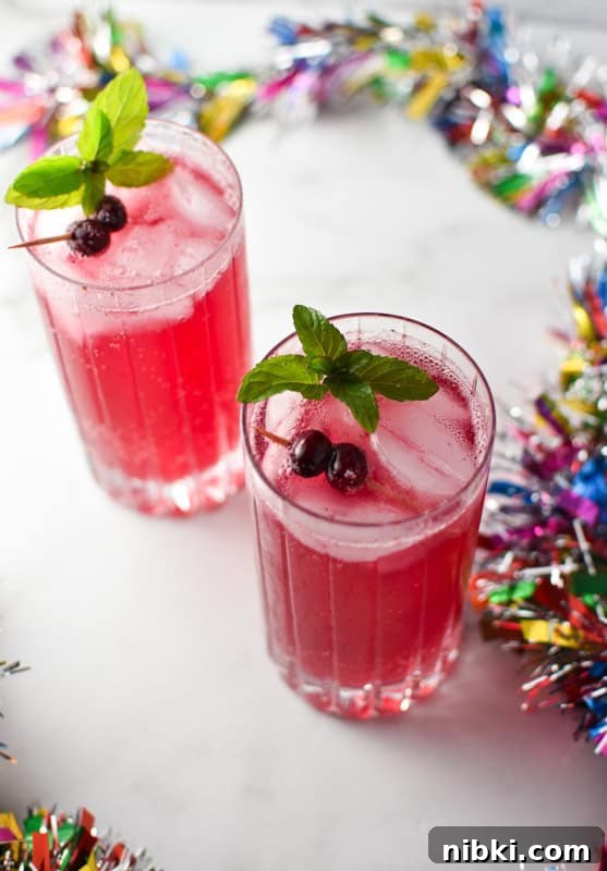 Two cocktail glasses filled with ice and a cranberry mocktail topped with cranberries and mint on a white marble surface
