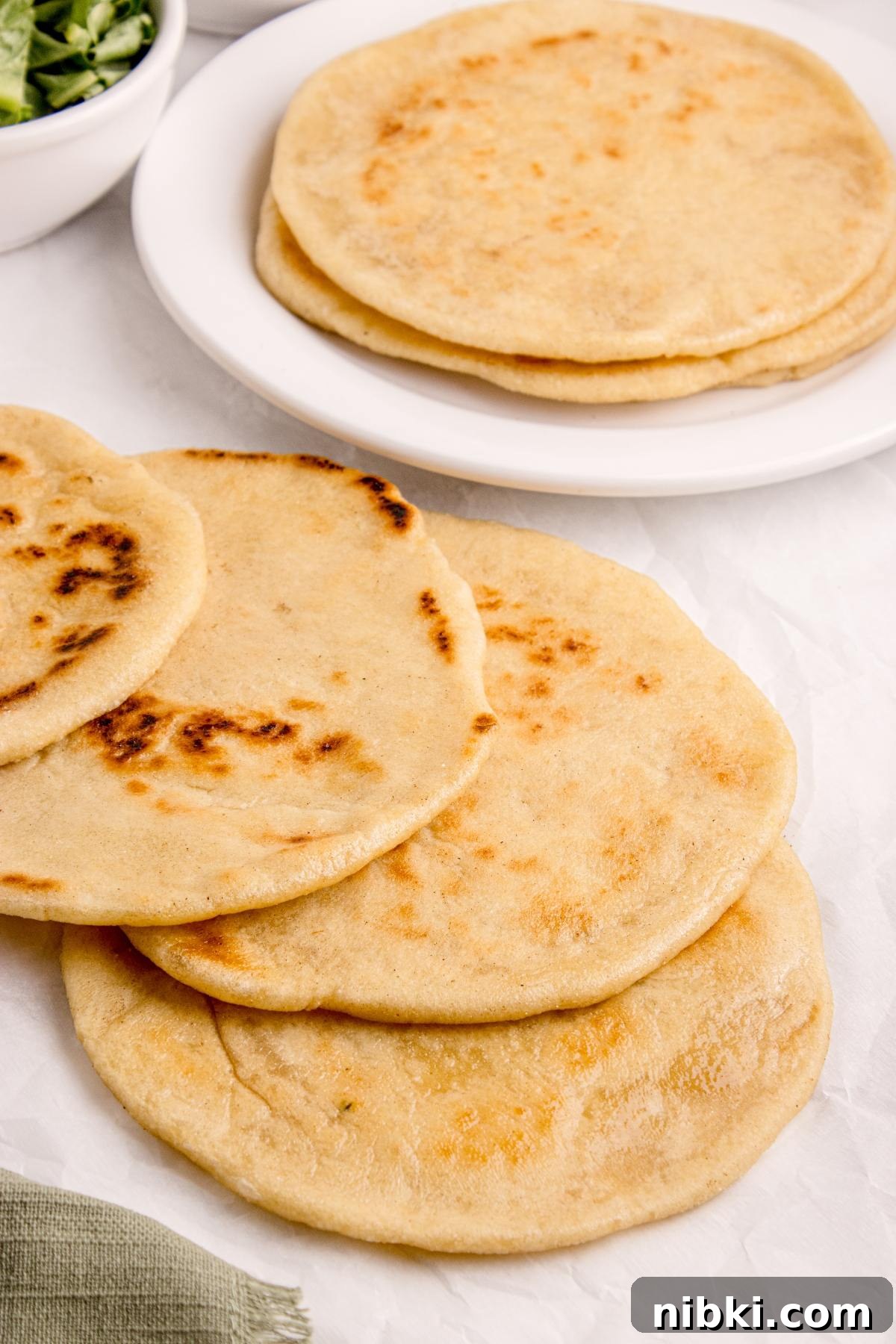 Several pieces of homemade pita bread, some stacked on a plate and others laid out on a white surface.
