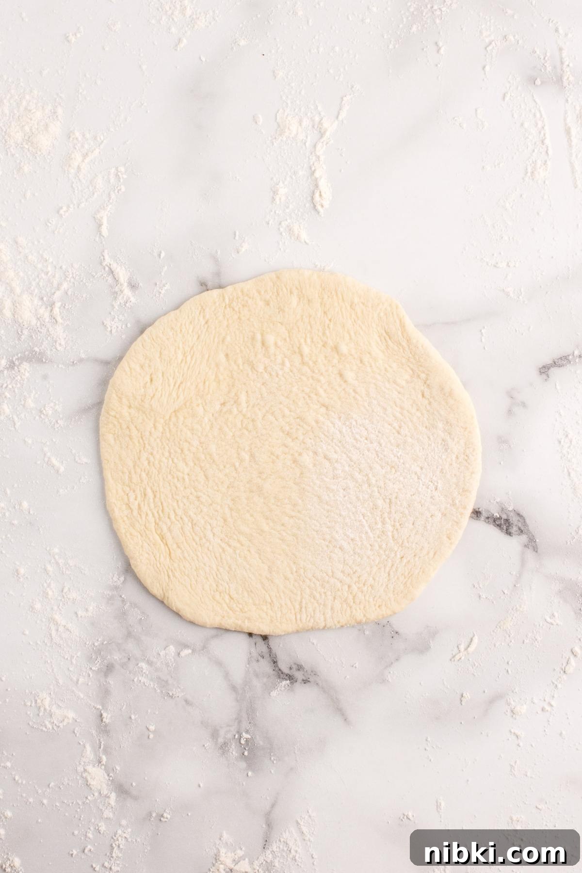 Round piece of pizza dough rolled out on a floured marble surface.
