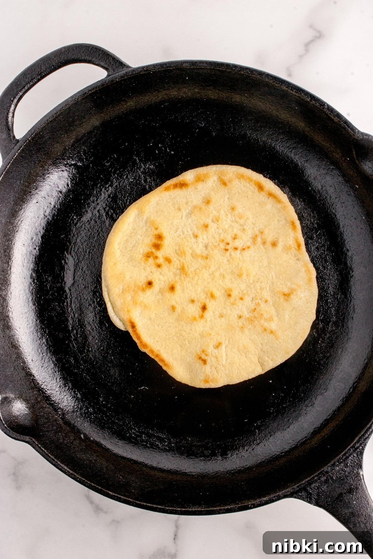 A round flatbread cooking on a black cast iron skillet with a white marble background.