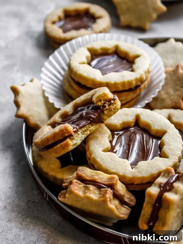 Nutella-Filled Linzer Cookies Recipe 3 filled Nutella Linzer cookies on serving platter - close up of cookie missing bite (3)