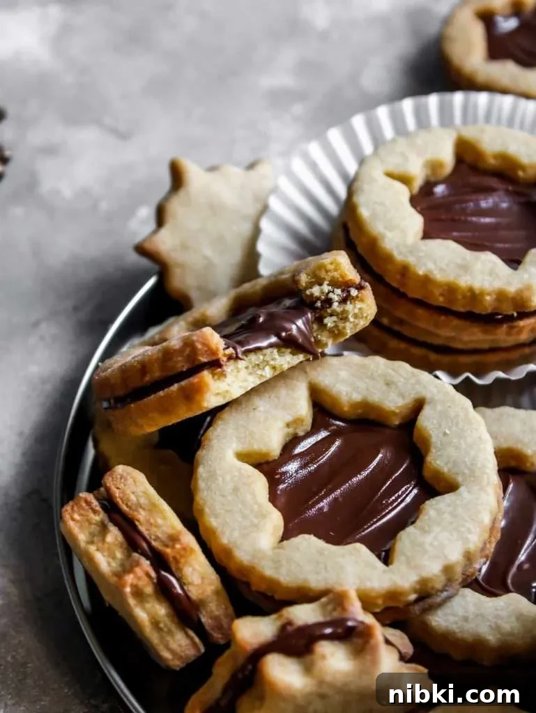 Nutella-Filled Linzer Cookies Recipe 11 filled Nutella Linzer cookies on serving platter - close up of cookie missing bite (1)