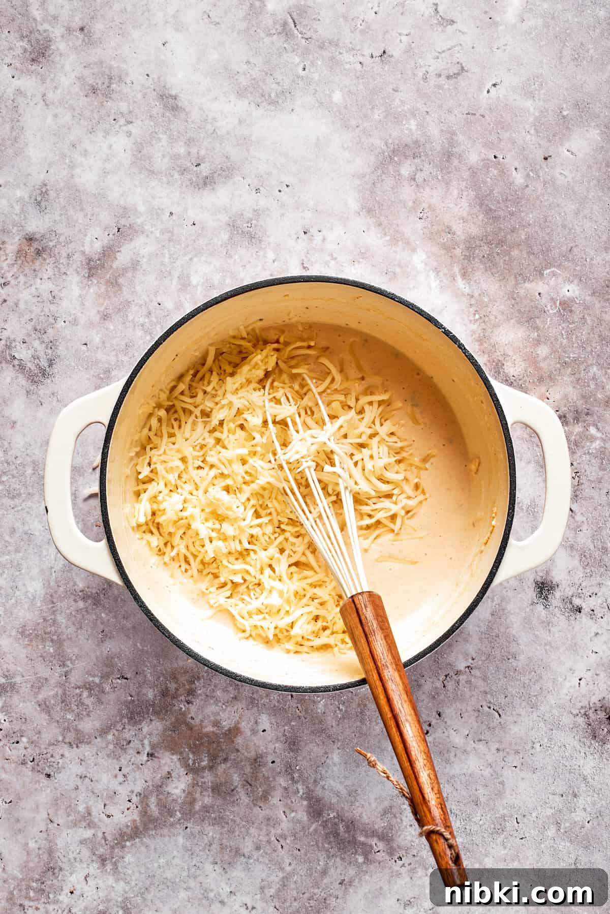 Shredded cheese is added to a pot of sauce.