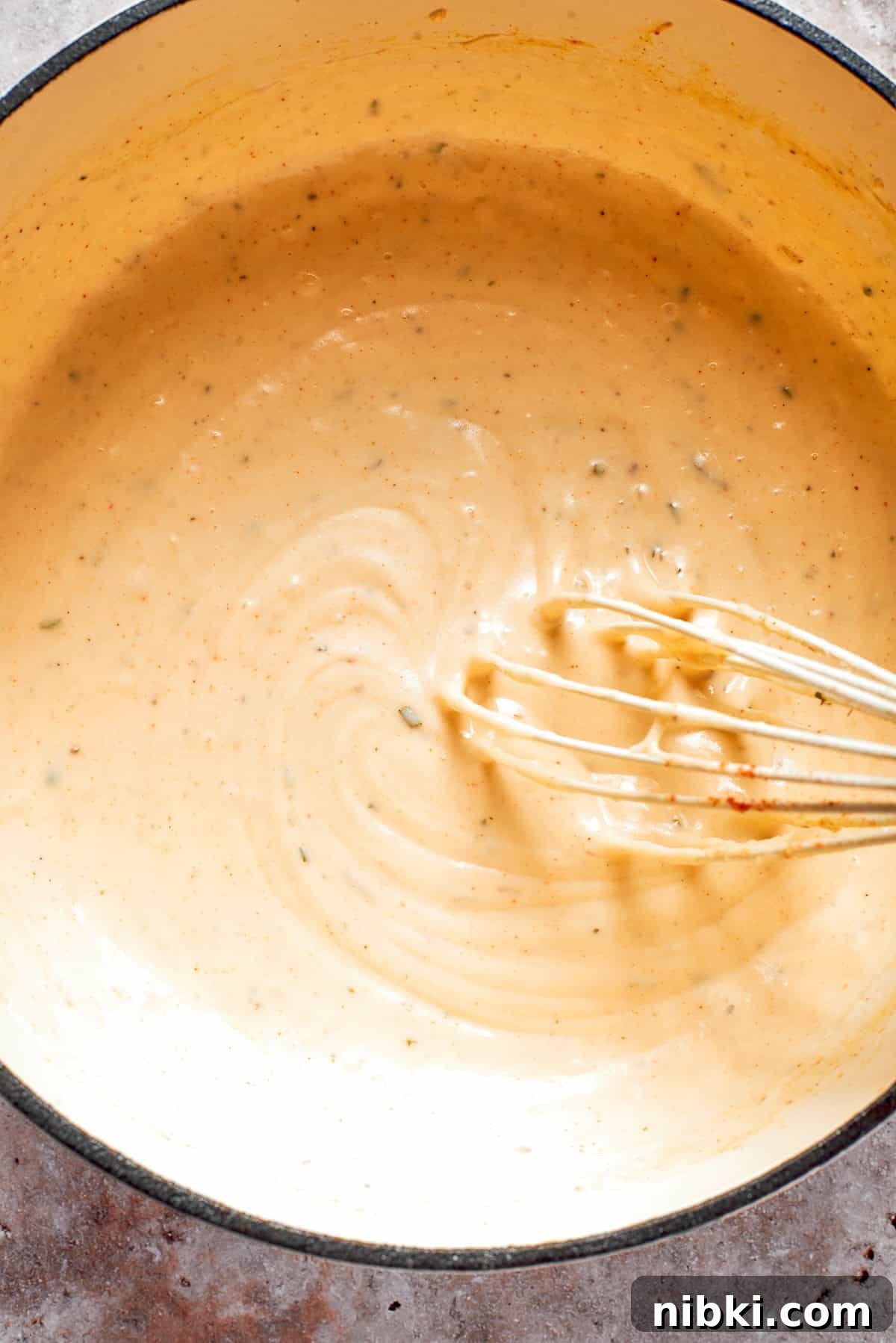 A whisk stirs a pot of cheese sauce.