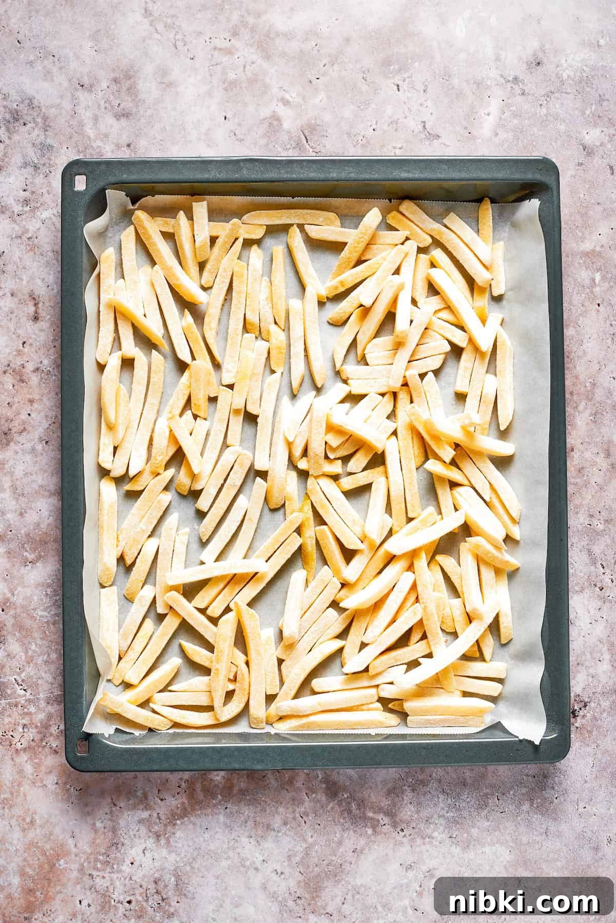 Frozen french fries spread out on a lined baking sheet.