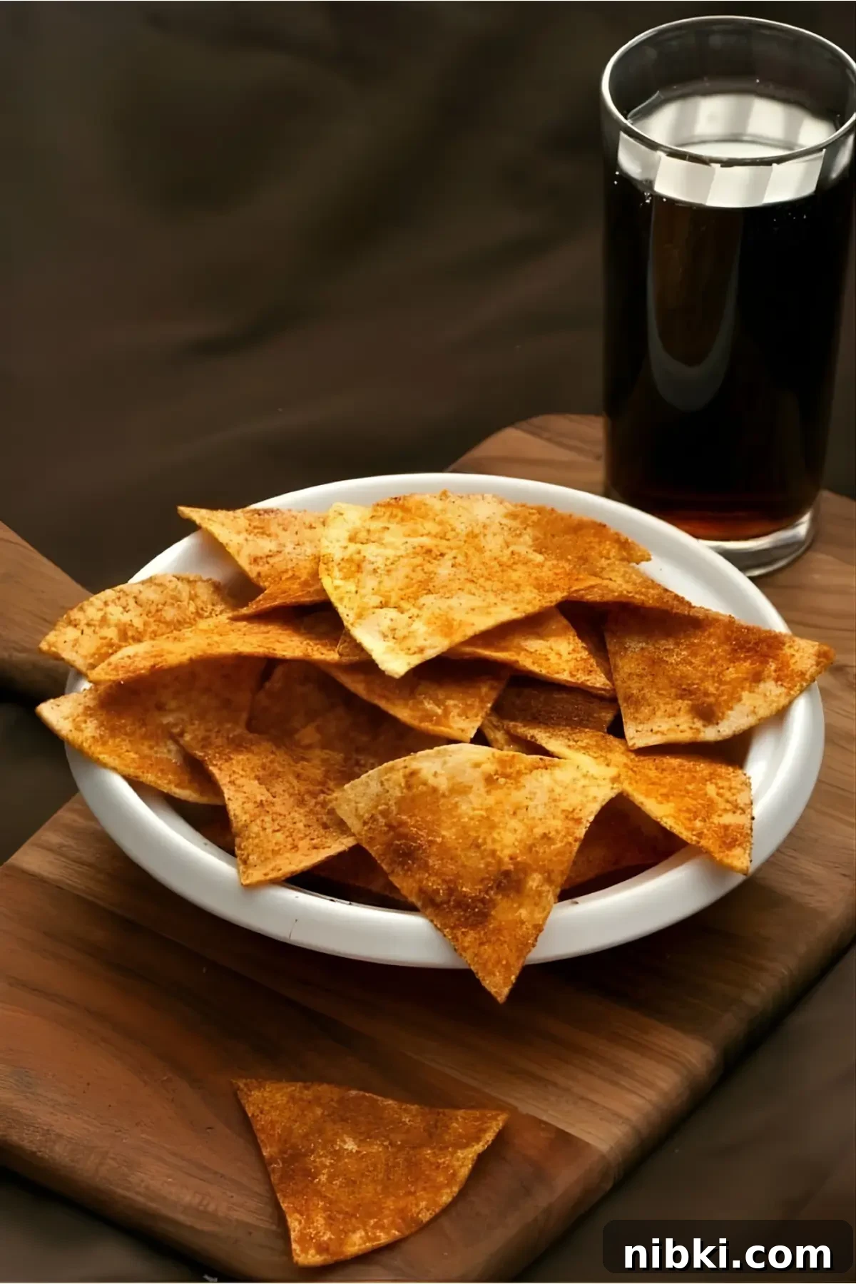 Bowl of seasoned DIY Doritos served with a glass of dark soda on a wooden board.