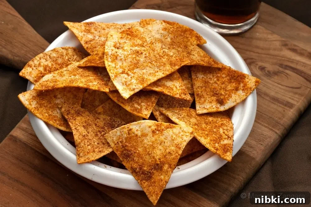 Homemade Doritos in a white bowl on a wooden board with a drink in the background.