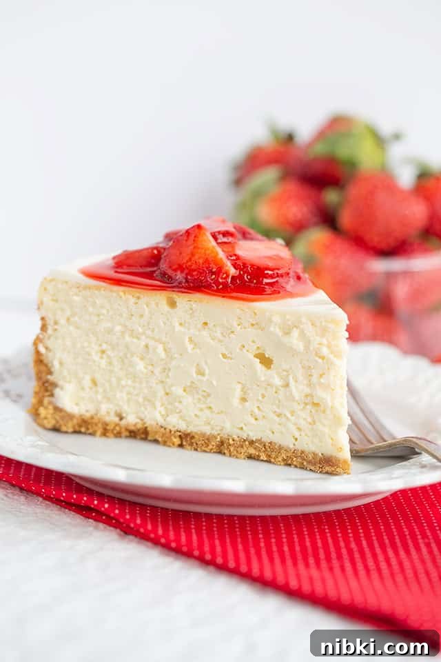 Classic Strawberry Cheesecake Recipe with Fresh Strawberries 3 A slice of strawberry cheesecake topped with sweet strawberry sauce sits on a white plate, with fresh strawberries in the background—a perfect strawberry dessert.