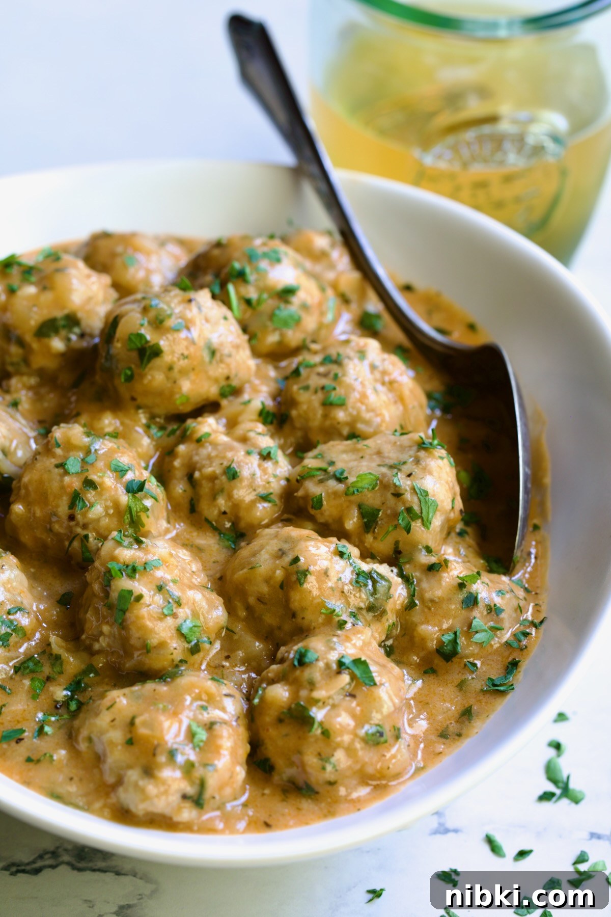 Oven-Baked Turkey Meatballs with Beer Glaze 2 Baked Turkey Meatballs in Beer - Onion Sauce in white oval bowl with serving spoon garnished with fresh parsley.
