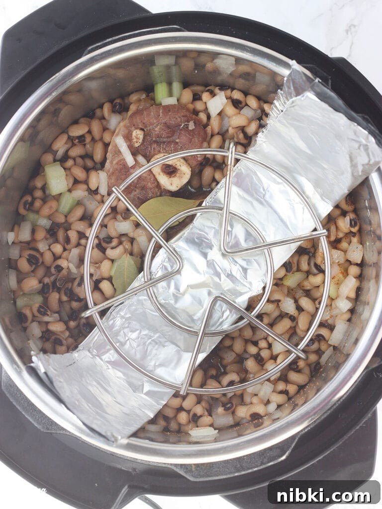 Instant Pot Hoppin' John: Southern Black-Eyed Peas and Rice 3 Overhead shot of an Instant Pot with black-eyed peas and ham hock under a trivet and foil sling