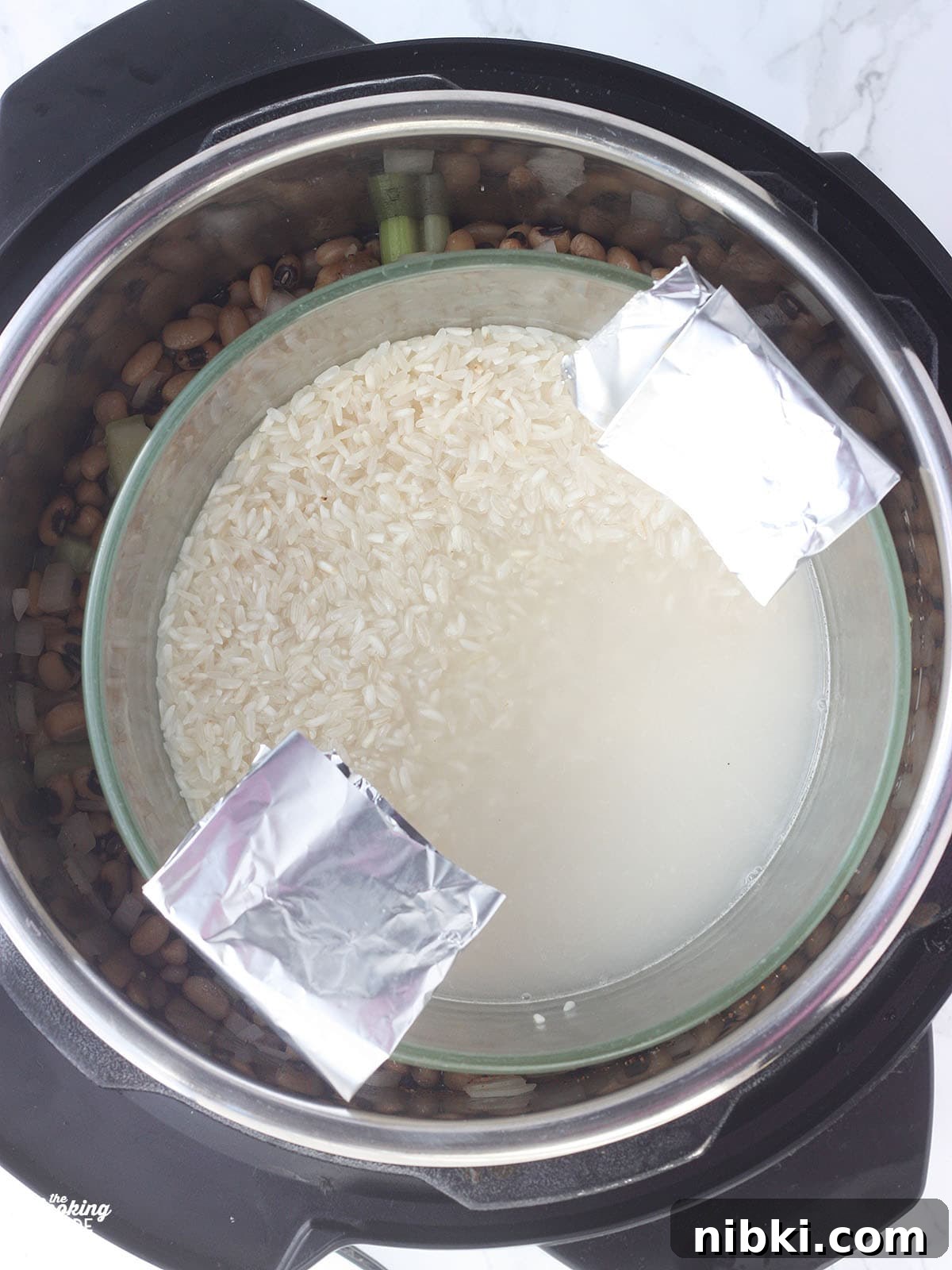 Instant Pot Hoppin' John: Southern Black-Eyed Peas and Rice 7 Overhead shot of a bowl of rice on a trivet in an Instant Pot with a foil sling folded over the sides.