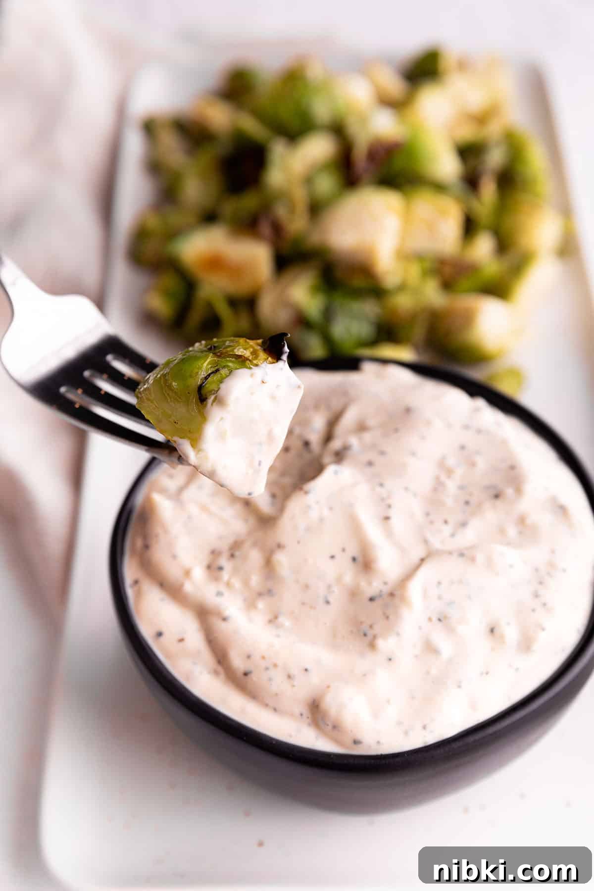 Homemade Lemon Garlic Aioli Recipe 2 A black bowl full of a lemon garlic aioli sauce and a fork dipping a brussels sprout into it.
