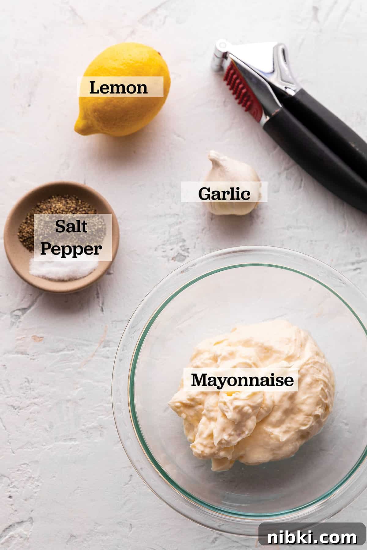 Homemade Lemon Garlic Aioli Recipe 3 A bowl with mayonnaise, a bowl with salt and pepper, a head of garlic and a lemon.