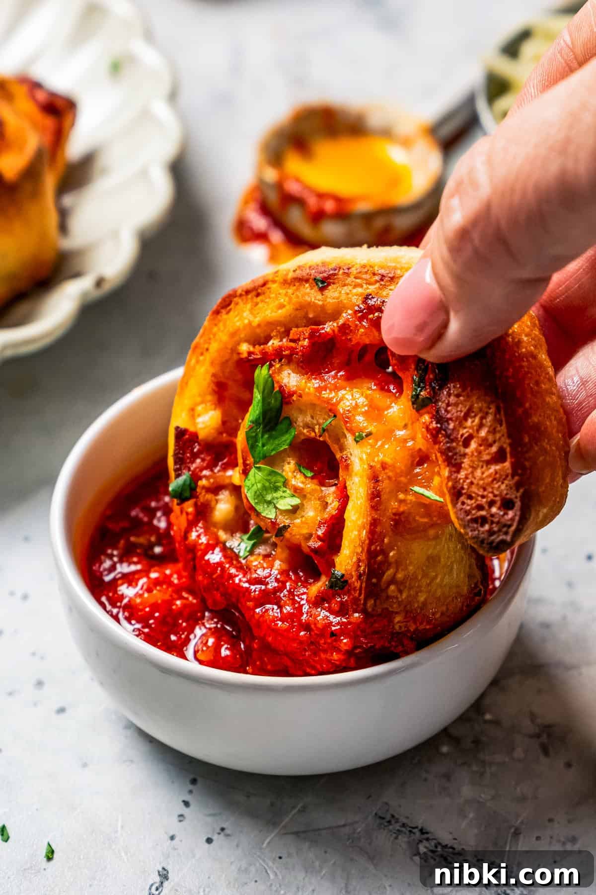 Cheesy pizza rolls are the easiest and best appetizer, made with flaky dough, tangy tomato sauce, melty mozzarella, and pepperoni. A hand dipping a pizza roll into a small bowl of marinara sauce.
