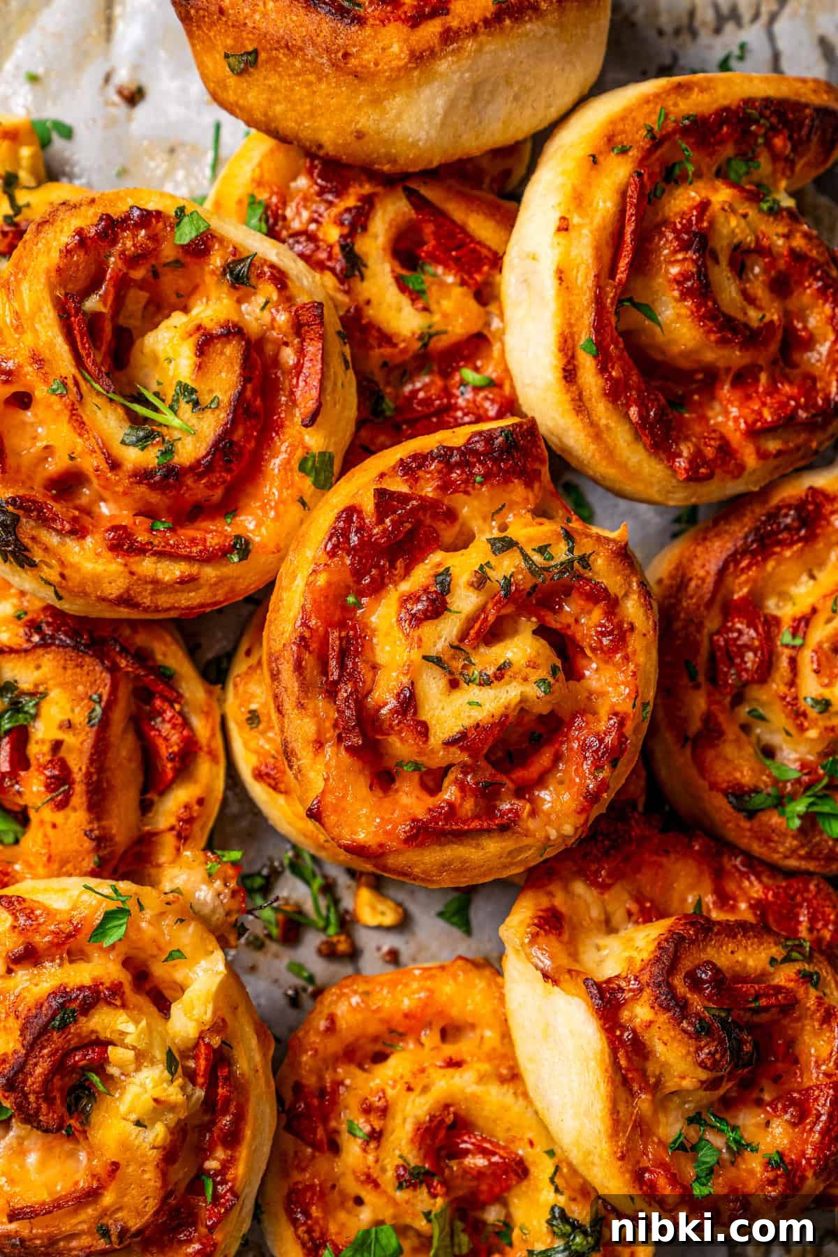 Cheesy pizza rolls are the easiest and best appetizer, made with flaky dough, tangy tomato sauce, melty mozzarella, and pepperoni. Close-up photo of assorted pepperoni pizza rolls piled on a counter.