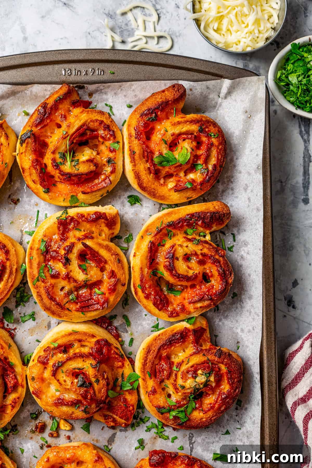 Cheesy pizza rolls are the easiest and best appetizer, made with flaky dough, tangy tomato sauce, melty mozzarella, and pepperoni. Overhead view of pepperoni pizza rolls on parchment-lined a baking sheet.