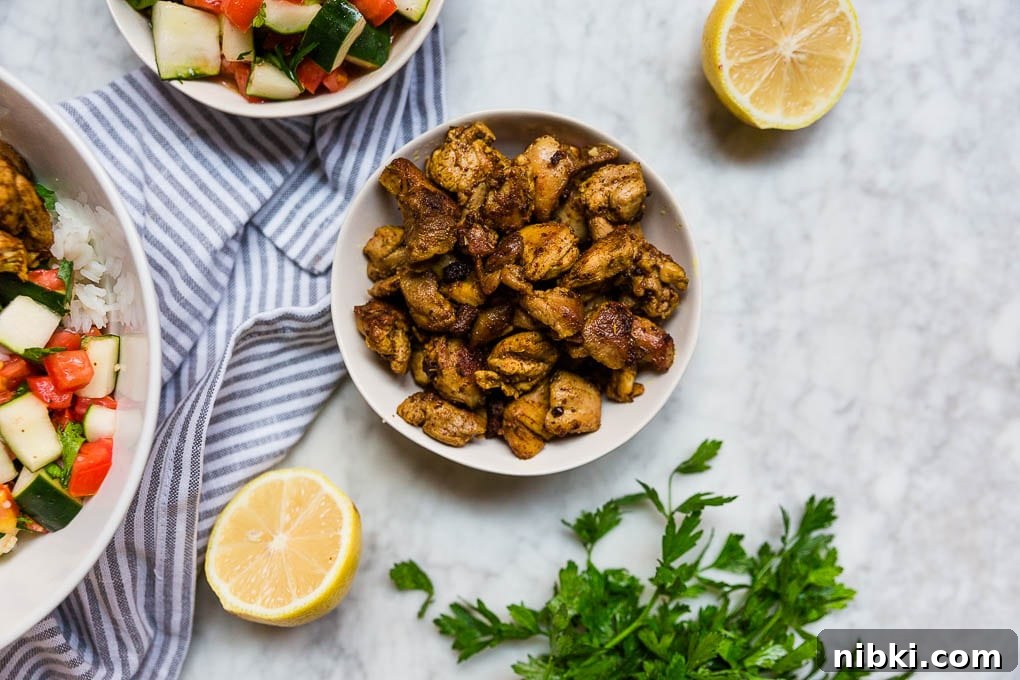 Mediterranean Chicken Bowls with Tzatziki and Quinoa 3 A bowl of spiced chicken thighs for easy mediterranean chicken bowls with lemon wedges, tomato cucumber salad and fresh parsley.