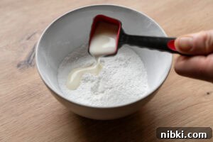 Pouring a tablespoon of milk into a bowl of icing sugar