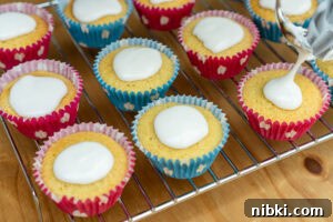 Fairy cakes on a wire rack with icing being put on top of each cake