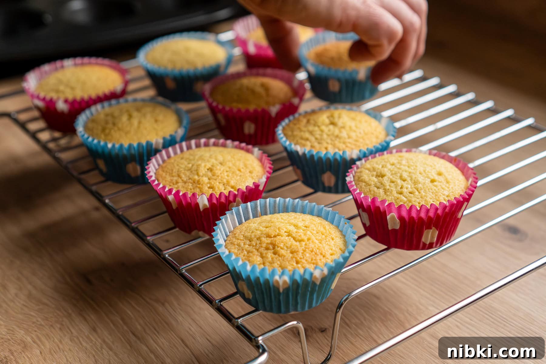 Placing cooked fairy cakes onto a wire rack to cool