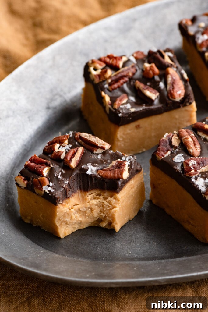 Piece of peanut butter fudge topped with chocolate and pecans, with a bite taken out of it.