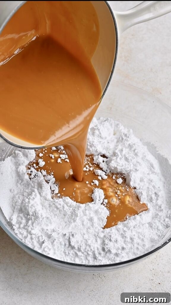 Melted peanut butter and butter being poured from saucepan into large bowl full of powdered sugar.