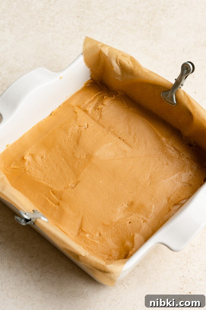 Peanut butter fudge in a parchment paper lined square baking dish.
