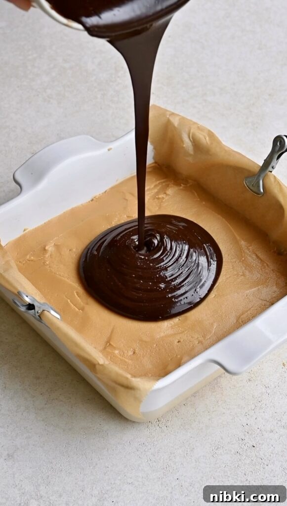 Chocolate ganache being poured onto peanut butter fudge in a pan.