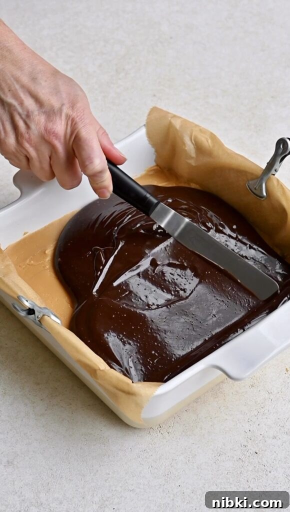 Chocolate ganache being spread over fudge with an offset spatula.