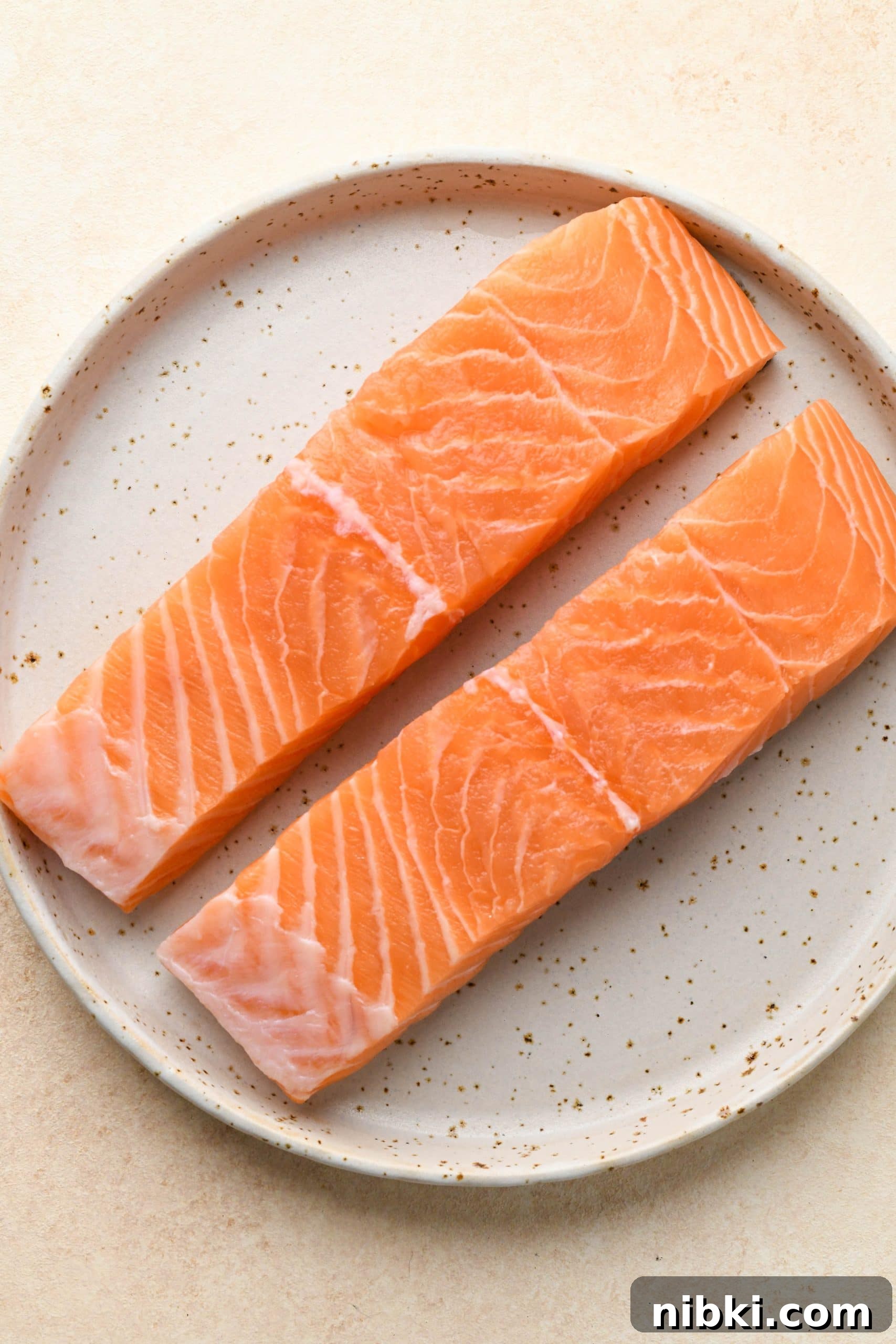 Two bright pink salmon filets on a white speckled plate.
