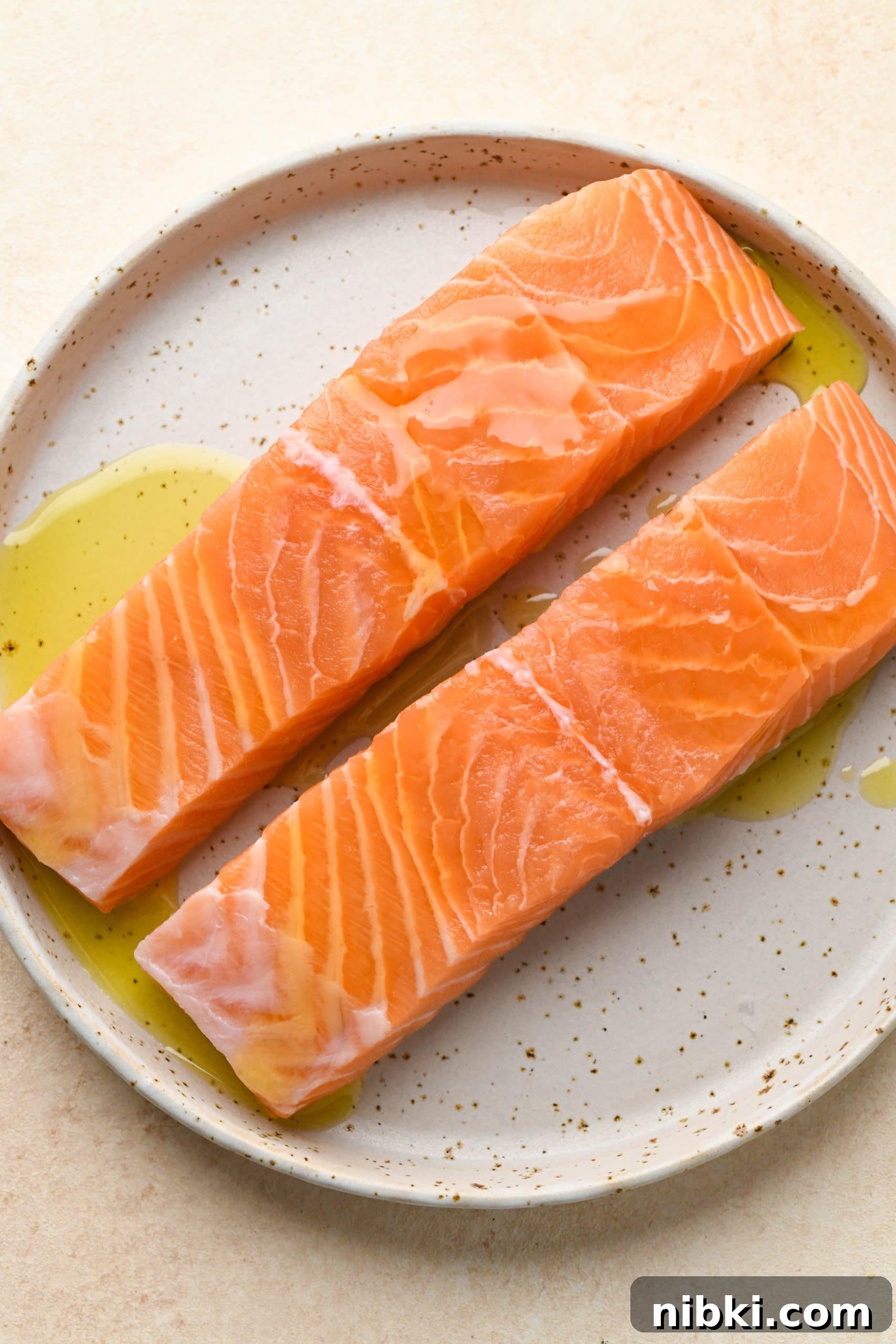 Raw salmon filets on a white speckled platter drizzled with avocado oil.
