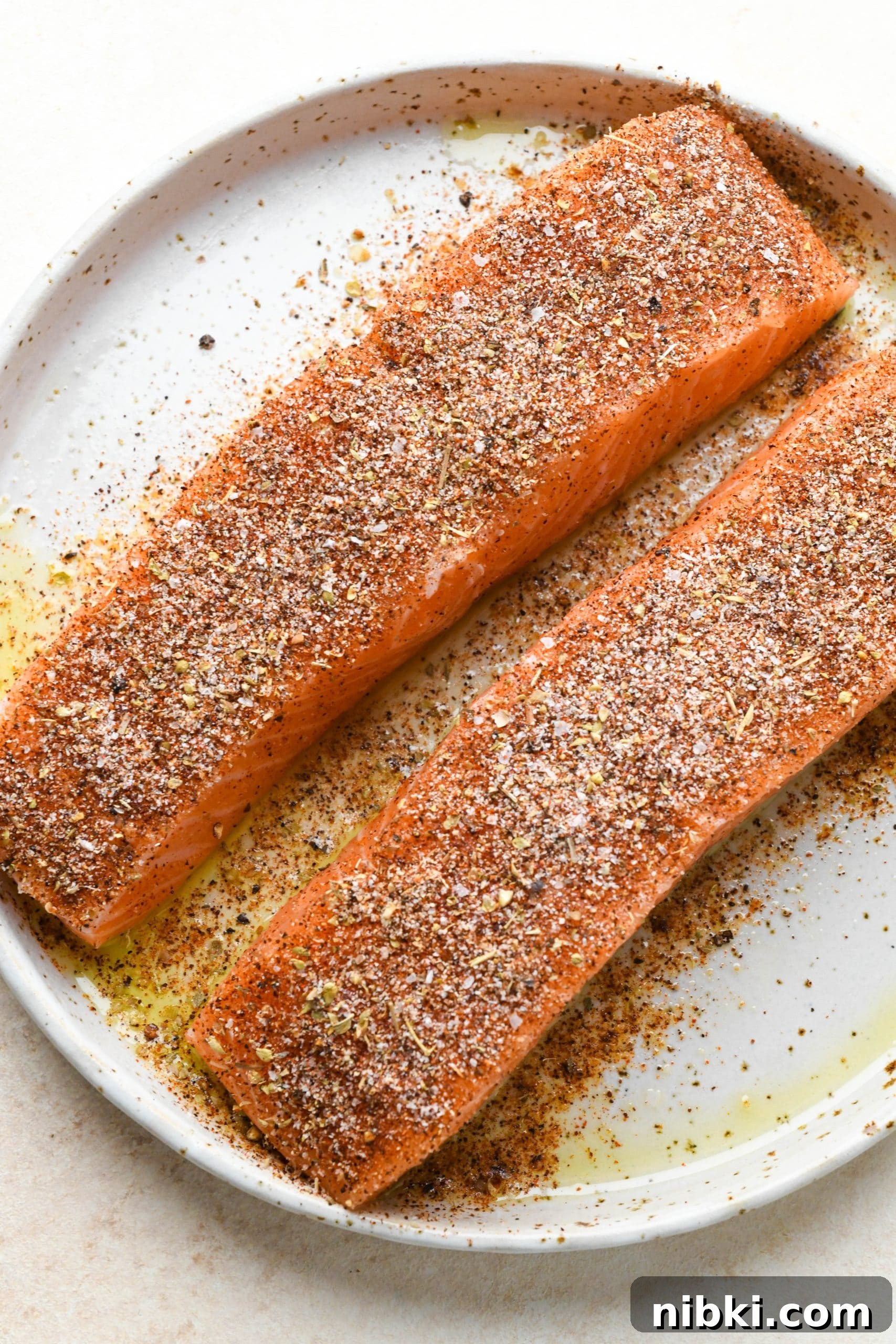 Raw salmon filets on a white speckled platter coated with avocado oil and blackening seasoning.