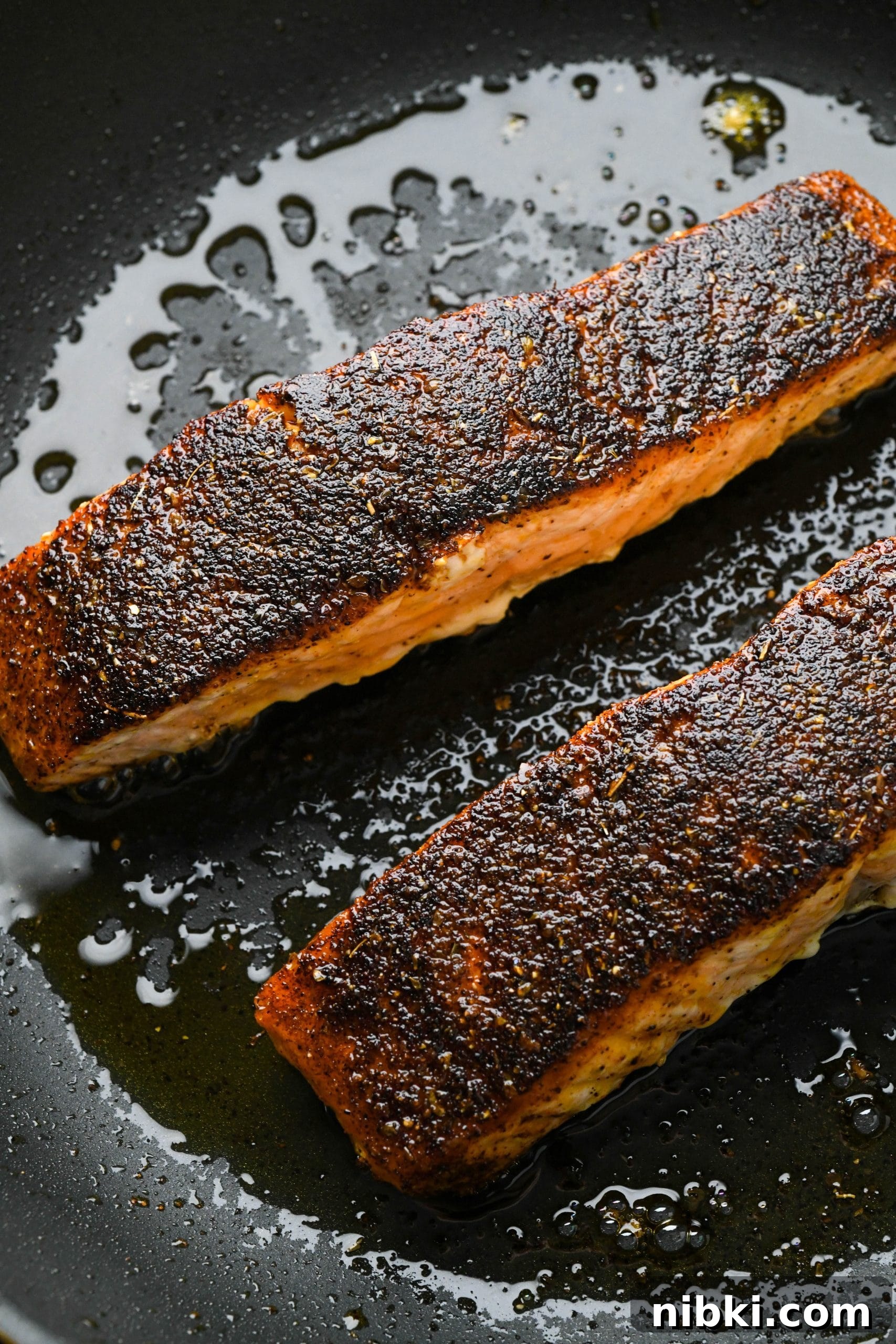 Cooked blackened salmon filets in a small skillet.