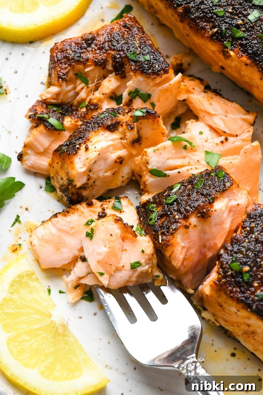 A fork with a bite of flaky blacked salmon resting on a plate.