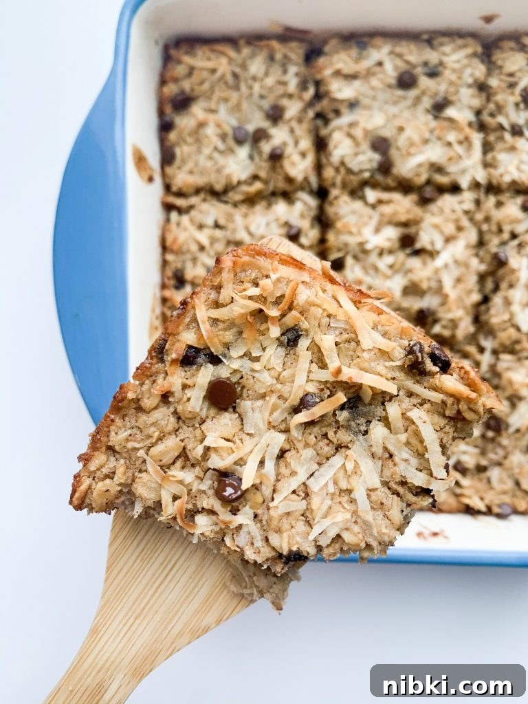 Almond Joy Inspired Chocolate Coconut Baked Oatmeal 3 a close up of a oatmeal square on a wooden spatula being held over the dish with the rest of the oatmeal