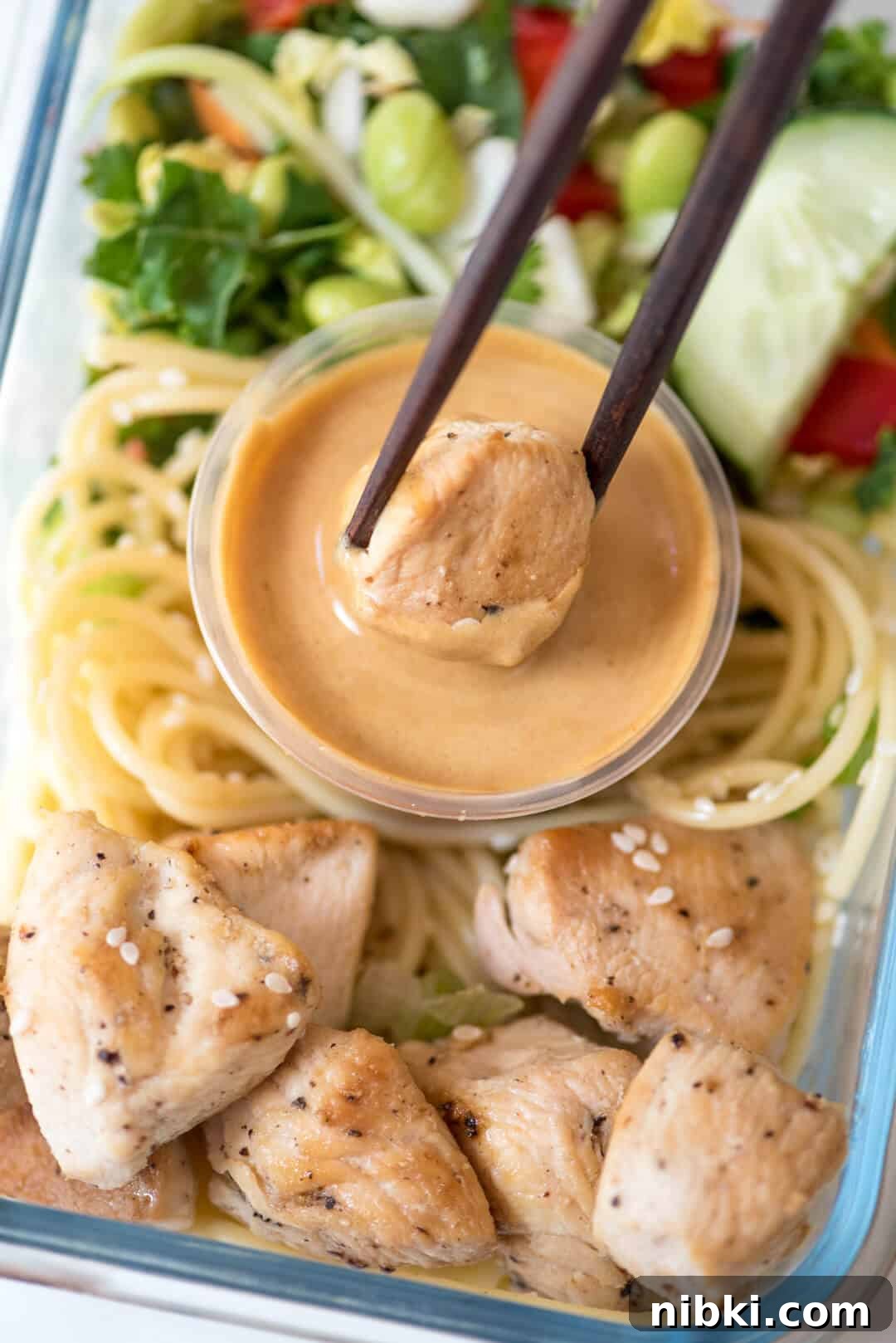 Chopsticks dip a piece of chicken into peanut sauce.