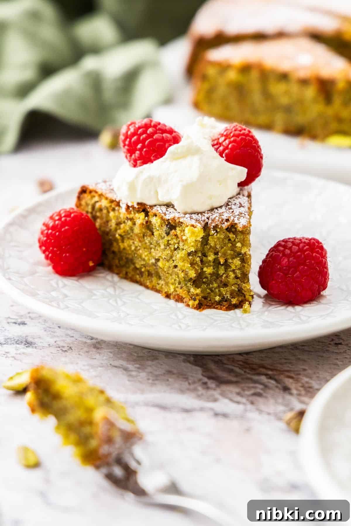 Decadent Flourless Pistachio Cake Recipe: Gluten-Free Dessert 7 Slice of Pistachio Cake with whipped cream and raspberries.