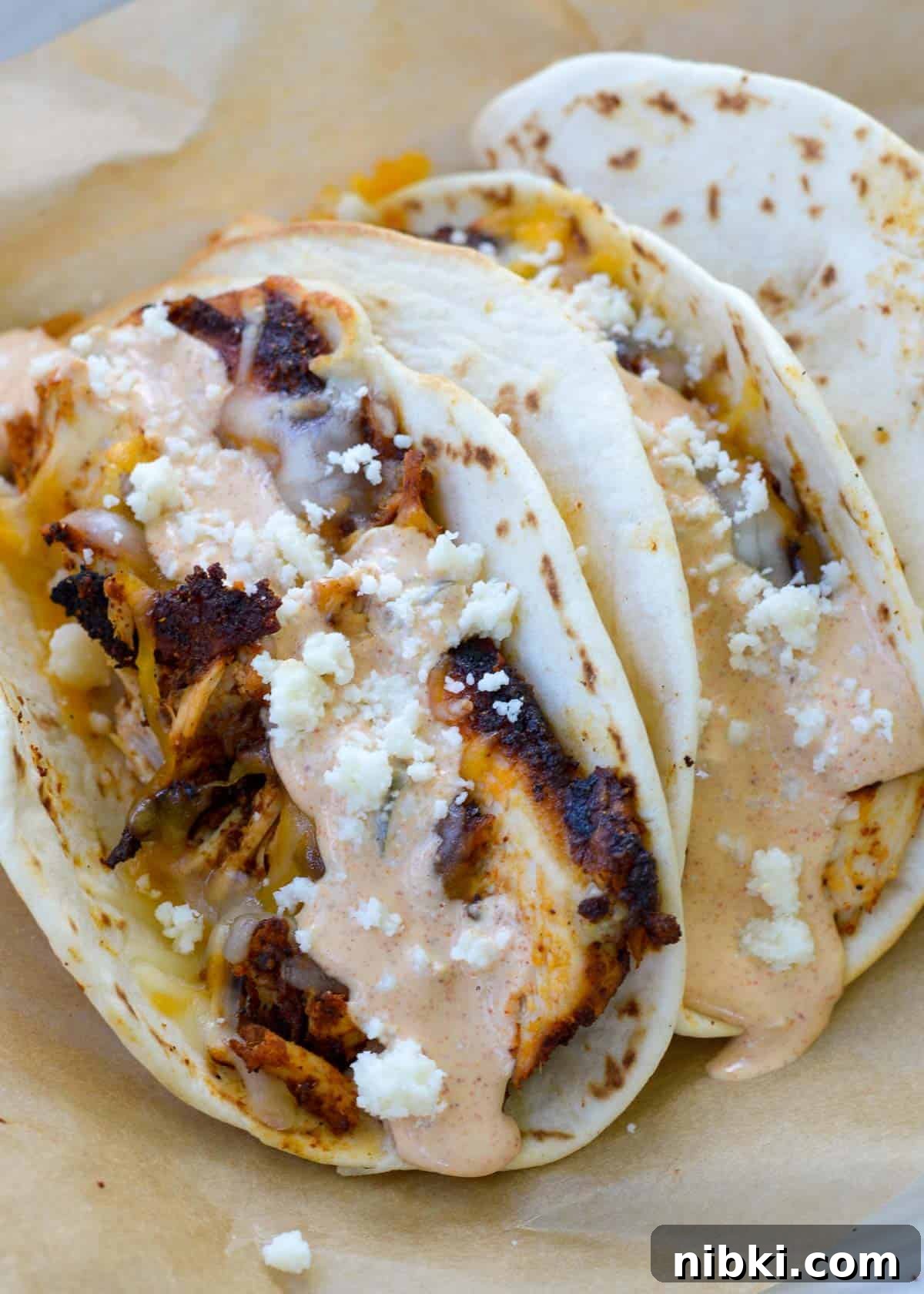 Copycat Taco Bell Creamy Jalapeno Sauce Recipe 3 Three delicious grilled chicken tacos with cheese, creamy jalapeno sauce, and flour tortillas on parchment paper