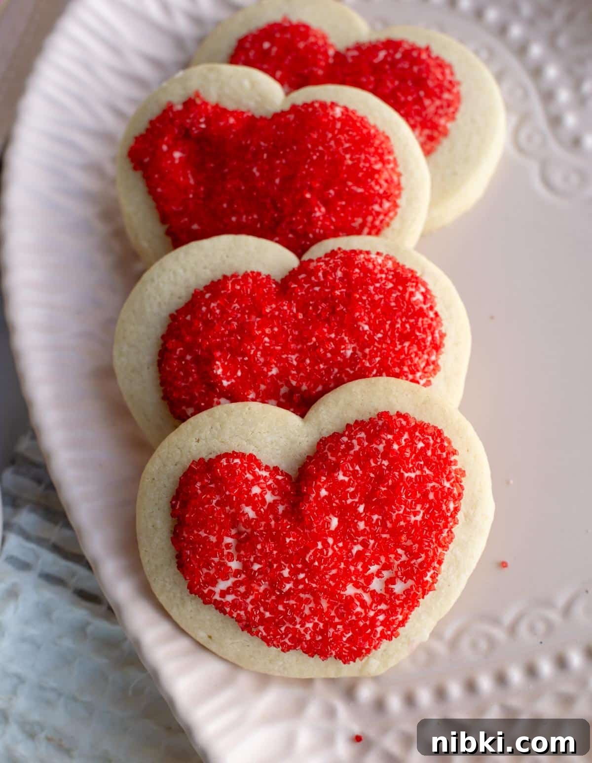 No-Chill Soft Sugar Cookies That Stay Tender and Chewy 2 A row of sugar cookies are layered on a white heart shaped plate.